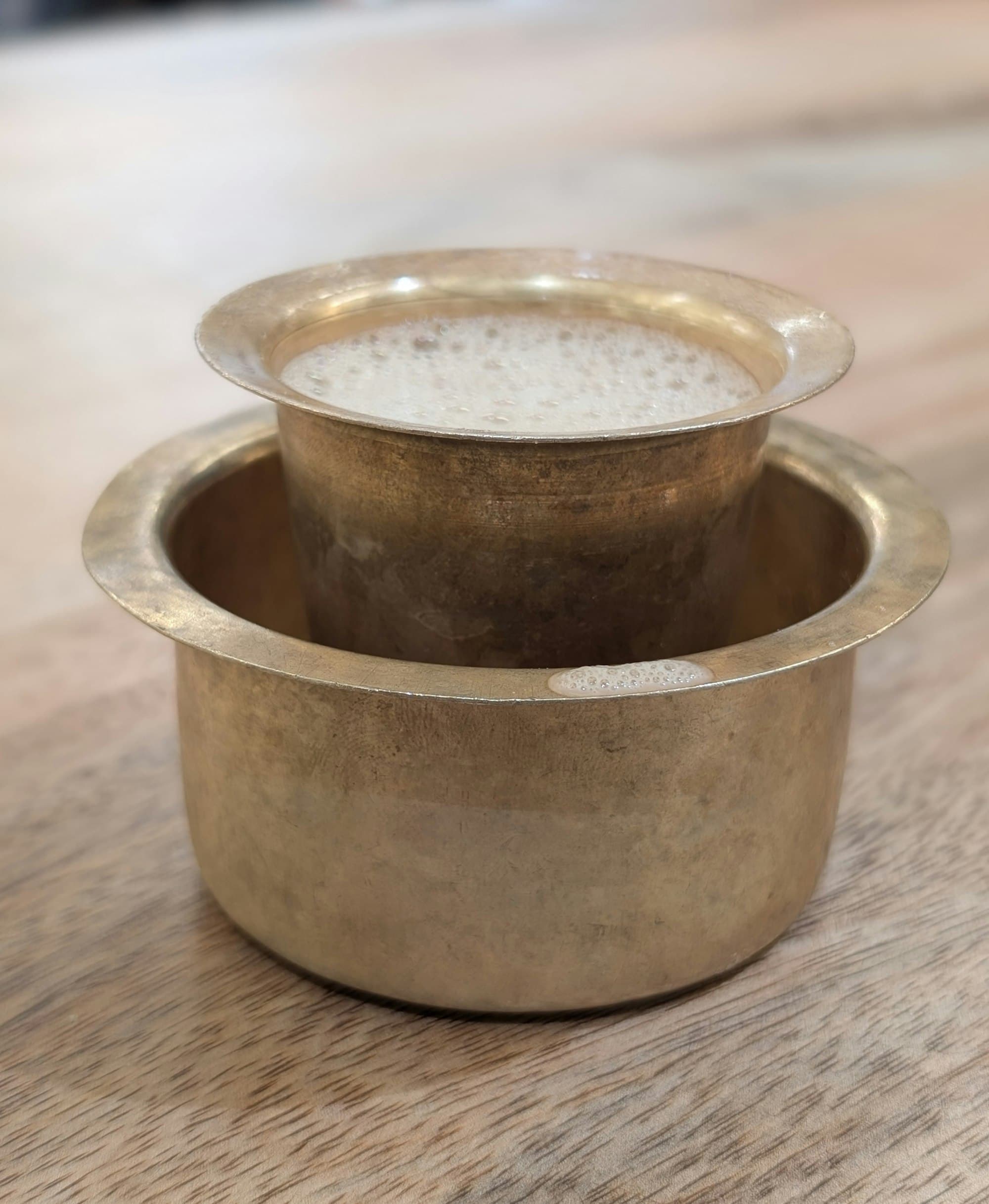 A traditional brass filter and a frothy tumbler of South Indian coffee