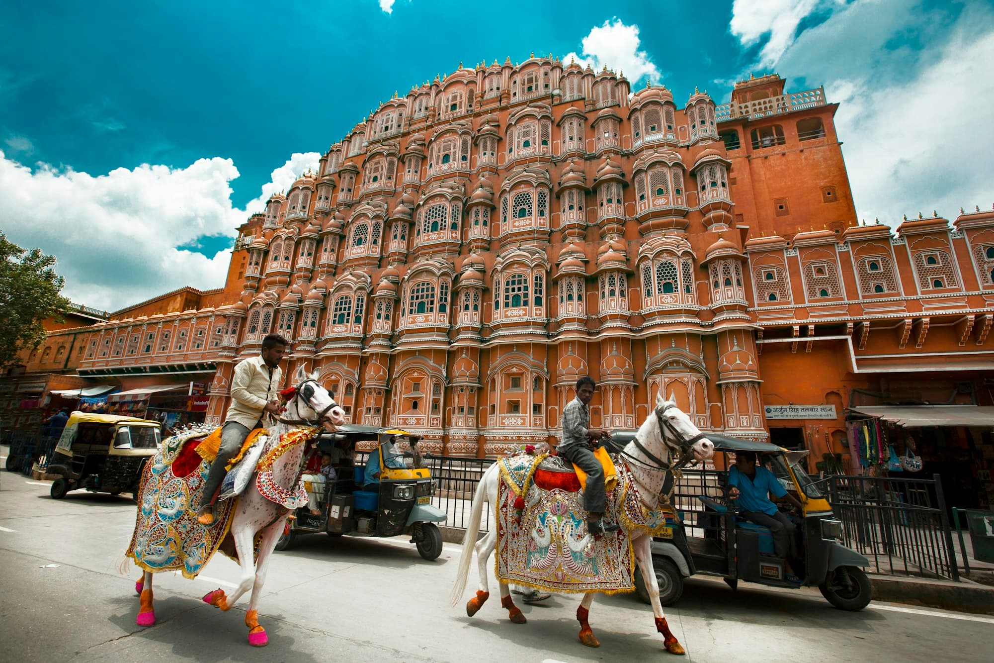 Two men on decorated white horses pass the Hawa Mahal in Jaipur