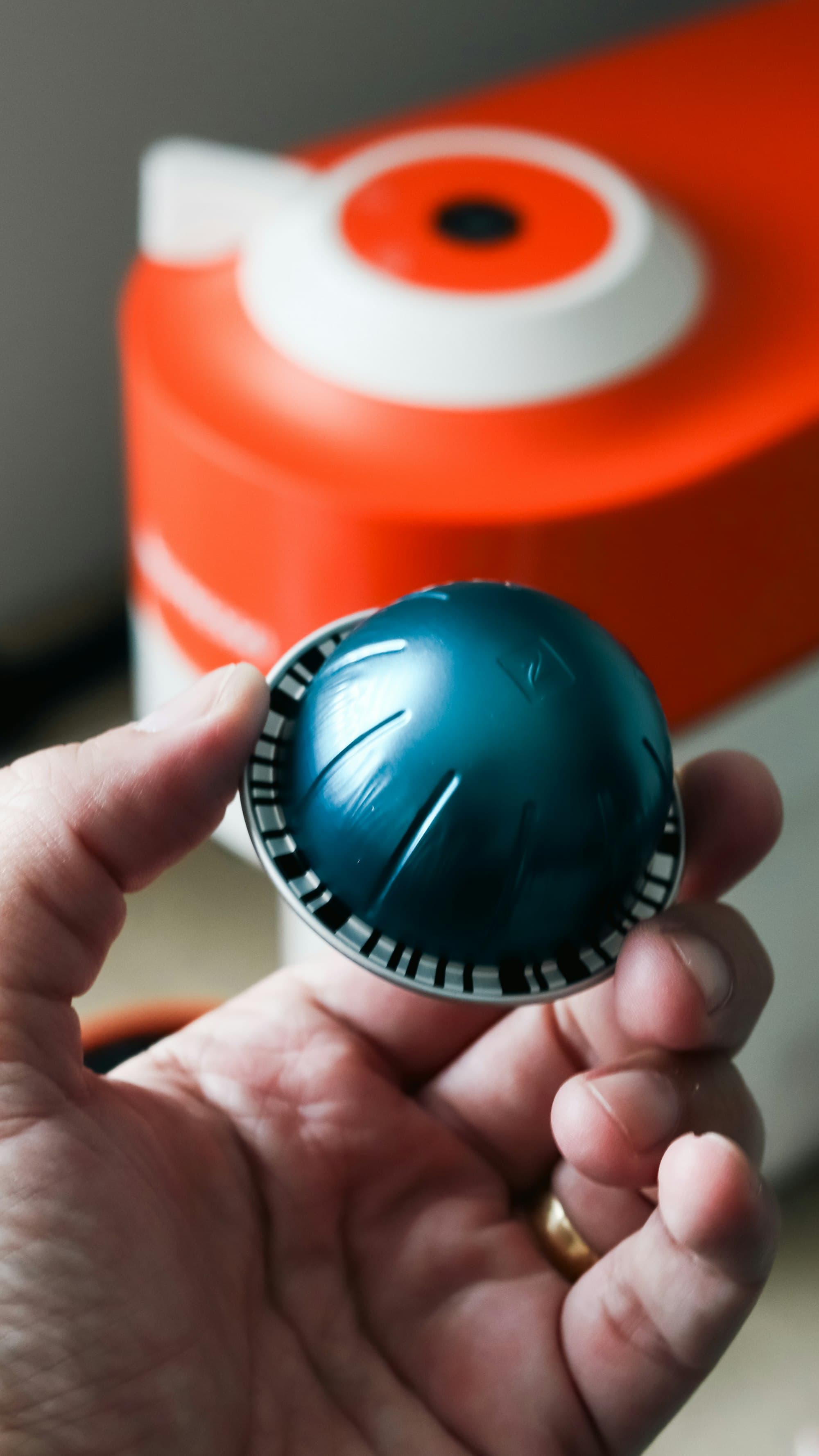 A hand holding a coffee capsule beside a capsule machine